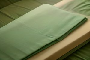 Folded sage green bamboo bedsheets on a bed